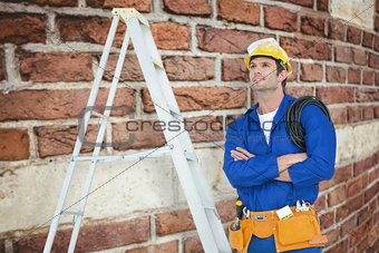 Composite image of thoughtful electrician with arms crossed by ladder