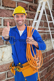 Composite image of male technician with wire roll gesturing thumbs up