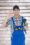 Composite image of plumber holding plunger while gesturing ok sign
