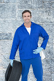 Composite image of mechanic holding tire while standing with hand on hip