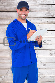 Composite image of portrait of happy male mechanic writing on clipboard