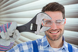 Composite image of confident repairman wearing protective glasses while holding wrench