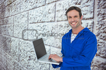 Composite image of handsome mechanic using laptop over white background