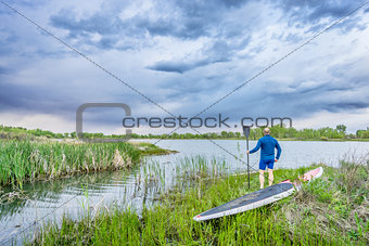 senior paddler with SUP paddleboar watching stormy sky