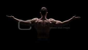 strong athletic mans back on dark background