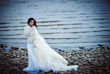 Beautiful sad girl in white dress standing on sea shore