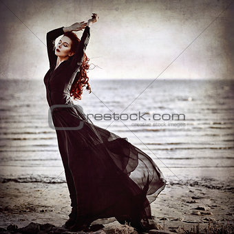 Beautiful goth girl standing on sea coast. Grunge texture effect