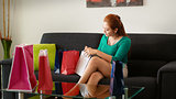 Latina Girl Peeps Into Shopping Bags On Sofa At Home