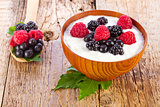 yogurt with wild berries in wooden bowl on wooden 