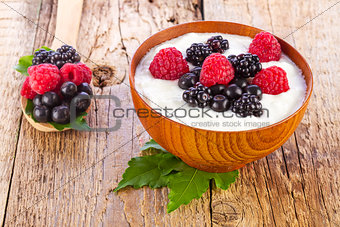 yogurt with wild berries in wooden bowl on wooden 