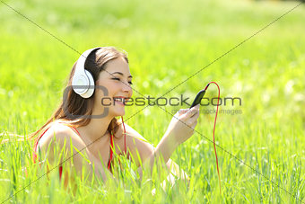 Girl listening music with headphones and smart phone in a field