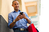 African American Man Text Messaging On Phone With Shopping Bags