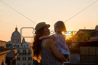 Mother in profile holding daughter in her arms overlooking Rome