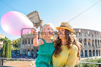 Smiling mother and daughter with pink balloon by Colosseum
