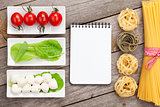 Tomatoes, mozzarella, pasta and green salad leaves with notepad 