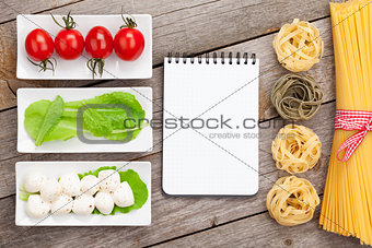 Tomatoes, mozzarella, pasta and green salad leaves with notepad 