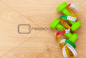 Dumbells and tape measure over wooden table with copy space