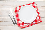 Empty plate, silverware and towel over wooden table background