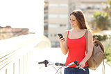 Woman using a smart phone walking with a bicycle