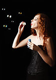 Beautiful redhead girl blows bubbles. Studio portrait, profile view