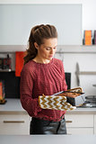 Woman standing in kitchen holding baking tin and looking down