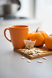 Pumpkin-coloured mug with miniature pumpkins and seeds on board