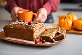 Closeup of fruit and seed loaf with woman's hands holding mug