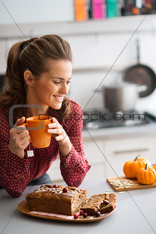 Woman smiling in kitchen holding mug with fresh fruit loaf