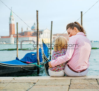 Mother and daughter sitting near gondolas in Venice