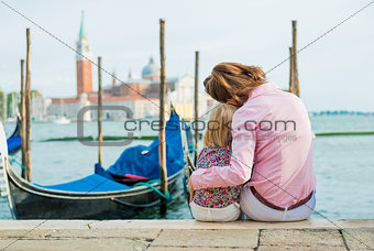Mother and daughter sitting together cuddling at water's edge