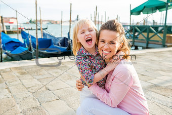 Happy mother kneeling down hugging playful daughter in Venice