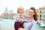 Smiling mother holding happy daughter in Venice on bridge