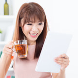 Asian girl drinking tea while using tablet