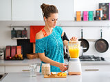 Fit woman in workout gear in kitchen making a smoothie