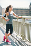 Smiling woman in workout gear standing on a bridge