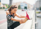 Woman runner stretching leg on rail in summer in urban setting