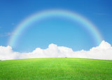 Green grass field, blue sky with clouds on horizon and rainbow