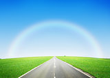 Road through the green field and sky with rainbow