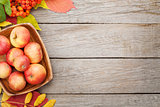 Apples in bowl and colorful autumn leaves on woden background