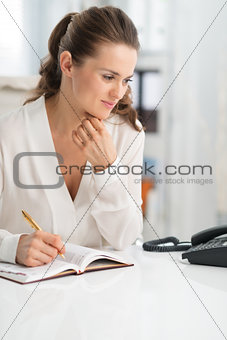 Pensive woman at work at desk, looking at telephone