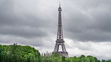 The Eiffel Tower over trees, stormy clouds