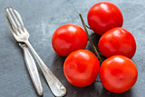 Red tomatoes on a branch, fork and knife.