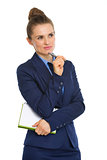 Businesswoman holding notebook and resting pen on chin, thinking