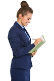 Smiling businesswoman in profile standing, writing in notebook