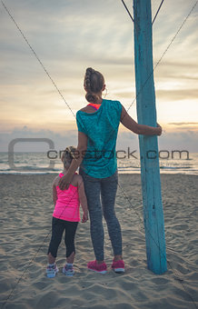 From behind, a mother and daughter in fitness gear at the beach