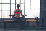 Rear view of woman on bench in lotus position in loft gym