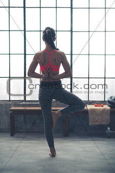 Rear view of woman doing yoga tree pose with hands behind back