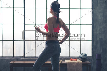 Fit woman standing in gym looking out window listening to music