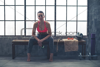 Woman sitting on bench by window in loft gym listening to music