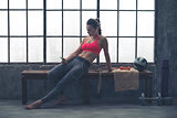 Fit woman in loft gym sitting on bench selecting music